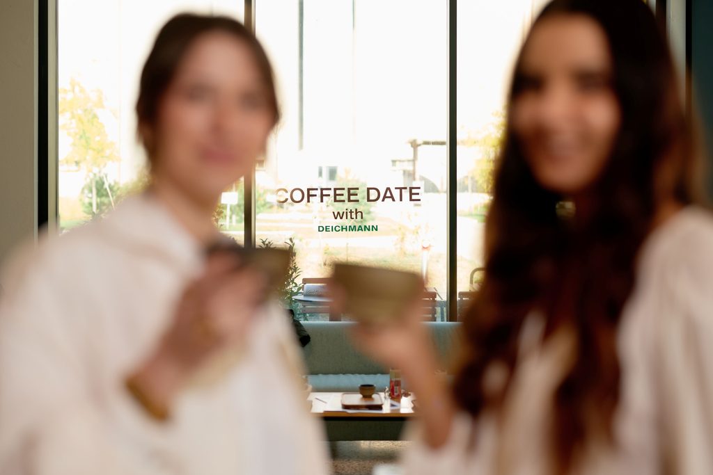 Dve gošće sa šoljicama kafe na Deichmann događaju, ispred natpisa Coffee Date with Deichmann.