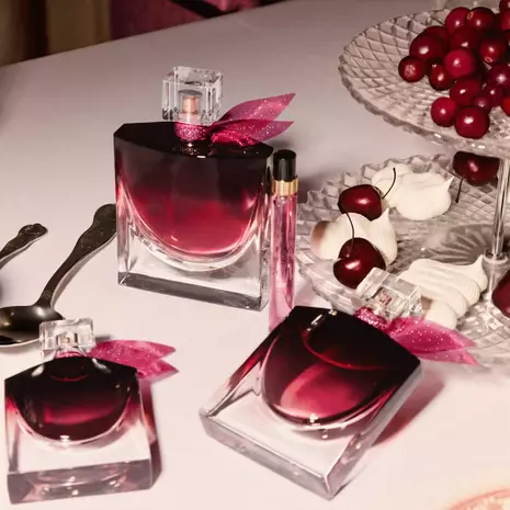 Tri bočice Lancôme La Vie Est Belle L’Elixir Very Cherry parfemske vode sa ružičastim mašnama, okružene trešnjama i puslicama.